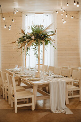 Restaurant, served table, rustic, huge compositions of flowers and tropical leaves on the table, plates, cutlery, crystal glasses, wooden chairs, garlands of light bulbs.