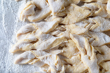 kitchen table. Sprinkled with flour. On it are dough products. Brushwood. Close-up