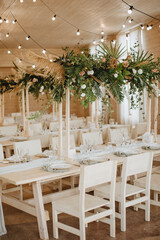 Restaurant, served table, rustic, huge compositions of flowers and tropical leaves on the table, plates, cutlery, crystal glasses, wooden chairs, garlands of light bulbs.