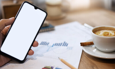 Close up of hand holding mobile phone with paperwork of investment and coffee drink on wooden table