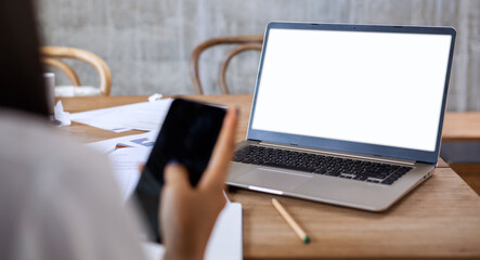 Selective focus of laptop monitor with blurred businesswoman in front using mobile phone. Concept working online from home