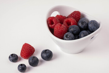 blueberries and raspberries in a cup on the table and next to the berries are scattered