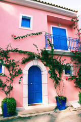 Fototapeta na wymiar Romantisches altes rosafarbenes Haus mit einer mit Blumen umgebenden Blauen Tür in einem griechischen Dorf
