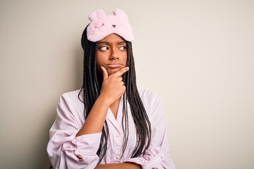 Young african american woman wearing pink pajama and sleep mask over isolated background with hand on chin thinking about question, pensive expression. Smiling with thoughtful face. Doubt concept.