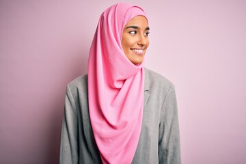 Young beautiful brunette businesswoman wearing pink muslim hijab and business jacket looking away...