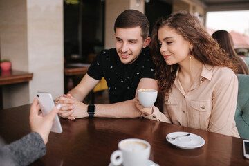 Group of tree friends on terrace. Yound people meeting in cafe. Friends sitting in cafe together. Female show to couple something on her smartphone
