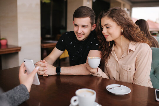 Group of tree friends on terrace. Yound people meeting in cafe. Friends sitting in cafe together. Female show to couple something on her smartphone