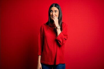Young beautiful brunette woman wearing casual sweater over isolated red background looking stressed...