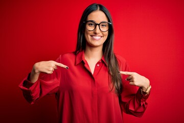 Young beautiful brunette woman wearing casual shirt and glasses over red background looking...