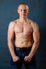 Obraz premium Portrait of strong healthy handsome Athletic Man Fitness Model posing near dark blue wall