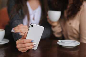 Two girls friend drink coffee in cafe and look in smat phone. Happy smiled women sittng on terrace. People look stories. Middle selection