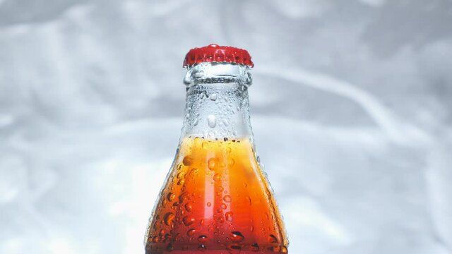 drink in glass bottle with flowing drops of water from ice closeup rotates on light background.