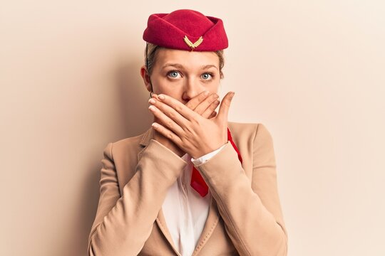 Young beautiful blonde girl wearing stewardess uniform shocked covering mouth with hands for mistake. secret concept.
