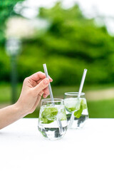 Beautiful glass of water or mojito with lime and mint cocktail on the gree background and white table summer vibe and atmosphere