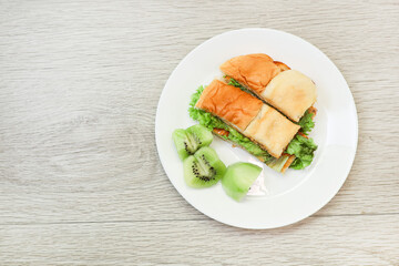 Top view of a plate of omelet sandwich with fruits on a wooden table.