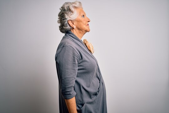 Senior beautiful grey-haired woman wearing casual dress standing over white background looking to side, relax profile pose with natural face and confident smile.