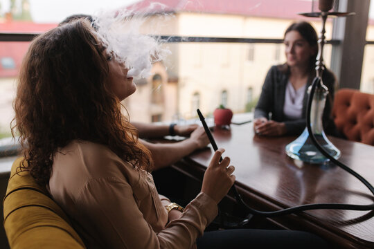 Group of people smoke hookah on terrace. Man and women meet in restaurant