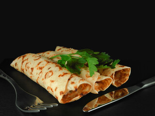 Rolled crepes (thin pancakes) with filling decorated with parsley leaves next to fork and knife on...