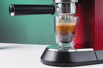 Red coffee machine. Transparent glass mug with fresh coffee. Coffee holder and cappuccino maker