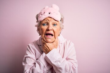 Senior beautiful woman wearing sleep mask and pajama over isolated pink background shouting and suffocate because painful strangle. Health problem. Asphyxiate and suicide concept.