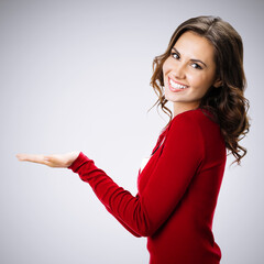 Studio portrait of happy brunette woman showing, holding something, over grey background with copy space. Square composition.
