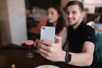Group of people smoke hookah on terrace. Man and women meet in restaurant. Man make stories while his girlfriend smoke. Man make selfie