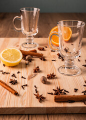 Obraz na płótnie Canvas Differential focus. Limpid empty glasses for mulled wine, anise flowers stars, nutmegs, cloves, fragrant cinnamon sticks, lemon and orange on structured natural wooden board, close up front view.
