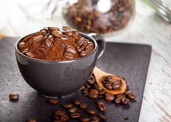 Ground coffee in a black cup, and at the top several roasted coffee beans.