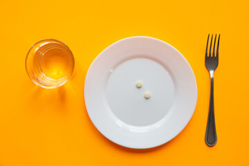 On the plate is a handful of pills, next to it is a glass of water and a fork