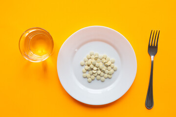 On the plate are two tablets, next to it is a glass of water and a fork