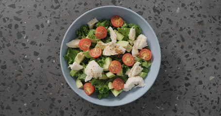 Top view salad with tomatoes , avocado, mozzarella and kale leaves in blue ceramic bowl on concrete background