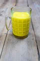 Golden milk in a glass cup on a wooden background