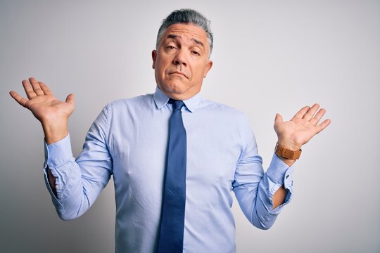 Middle age handsome grey-haired business man wearing elegant shirt and tie clueless and confused expression with arms and hands raised. Doubt concept.