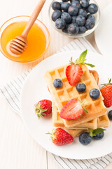 Photo of fresh homemade food made of Belgian waffles with honey, chocolate, strawberry, blueberry. Healthy dessert breakfast concept. 