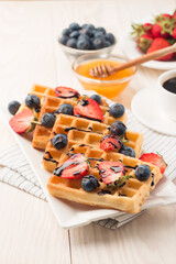 Photo of fresh homemade food made of Belgian waffles with honey, chocolate, strawberry, blueberry. Healthy dessert breakfast concept. 