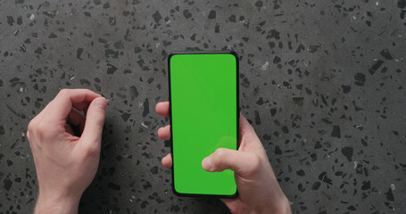 Top view man hand use smartphone with green screen on concrete background
