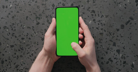 Top view man hand use smartphone with green screen on concrete background