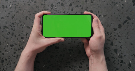 Top view man hand show smartphone with green screen on concrete background