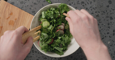 Naklejka na ściany i meble Top view man hands mix salad from radish, cucumbers, kale salad and herbs with dressing