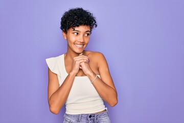 Young beautiful african american afro woman wearing casual t-shirt over purple background laughing nervous and excited with hands on chin looking to the side