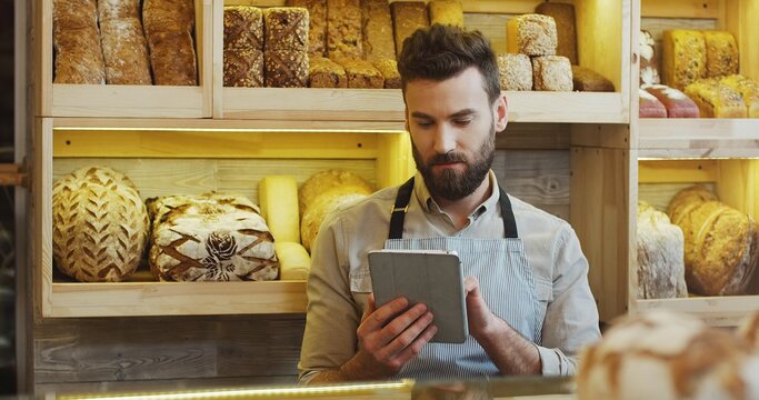 Portrait of male baker working in in bakery shop and using tablet