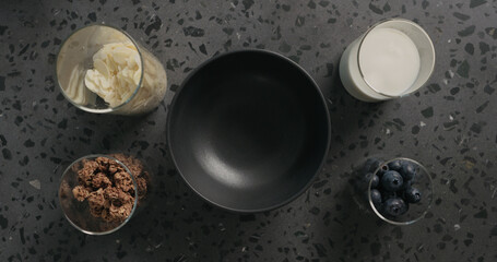breakfast with chocolate granola, almond flakes and blueberry in black bowl on terrazzo surface