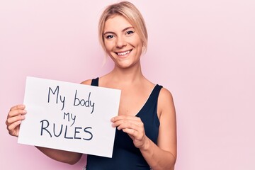 Young blonde woman asking for women freedom holding paper with my body my rules message looking positive and happy standing and smiling with a confident smile showing teeth