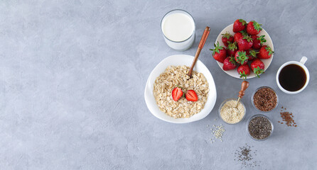 Obraz na płótnie Canvas Ingredients for healthy breakfast concept banner. Bowl of oatmeal porridge, strawberries, milk and seeds on stone background with copy space