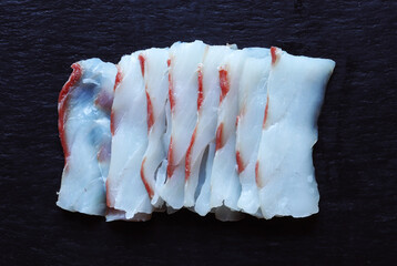 Photography of a filet of meagre cut like sashimi on slate background for food illustrations