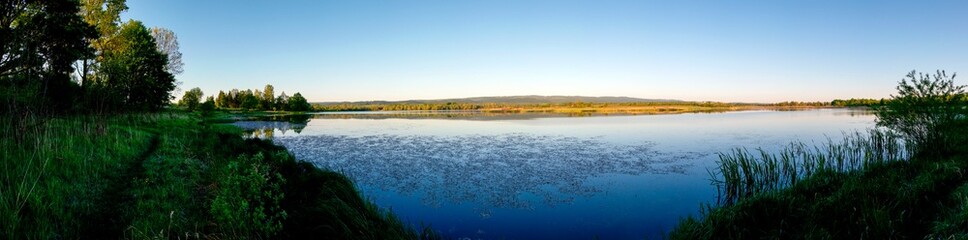 Panoramic landscape from the lake shore with colorful clouds in the spring sun.