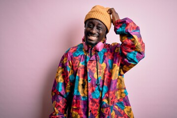 Obraz premium Young handsome african american man wearing colorful coat and cap over pink background confuse and wonder about question. Uncertain with doubt, thinking with hand on head. Pensive concept.