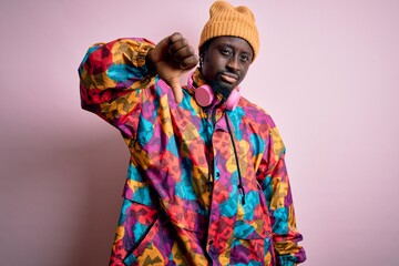 Obraz premium Young handsome african american man wearing colorful coat and cap over pink background looking unhappy and angry showing rejection and negative with thumbs down gesture. Bad expression.