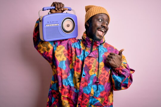 Young african american man listening to music holding portable vintage retro radio pointing and showing with thumb up to the side with happy face smiling