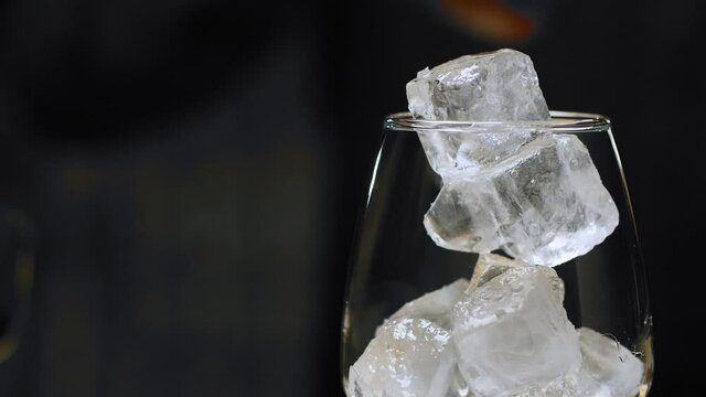 Making an Aperol Spritz Cocktail. Close up bartenders hands pouring aperol and prosecco in wine glass with ice. Long fizzy drink.